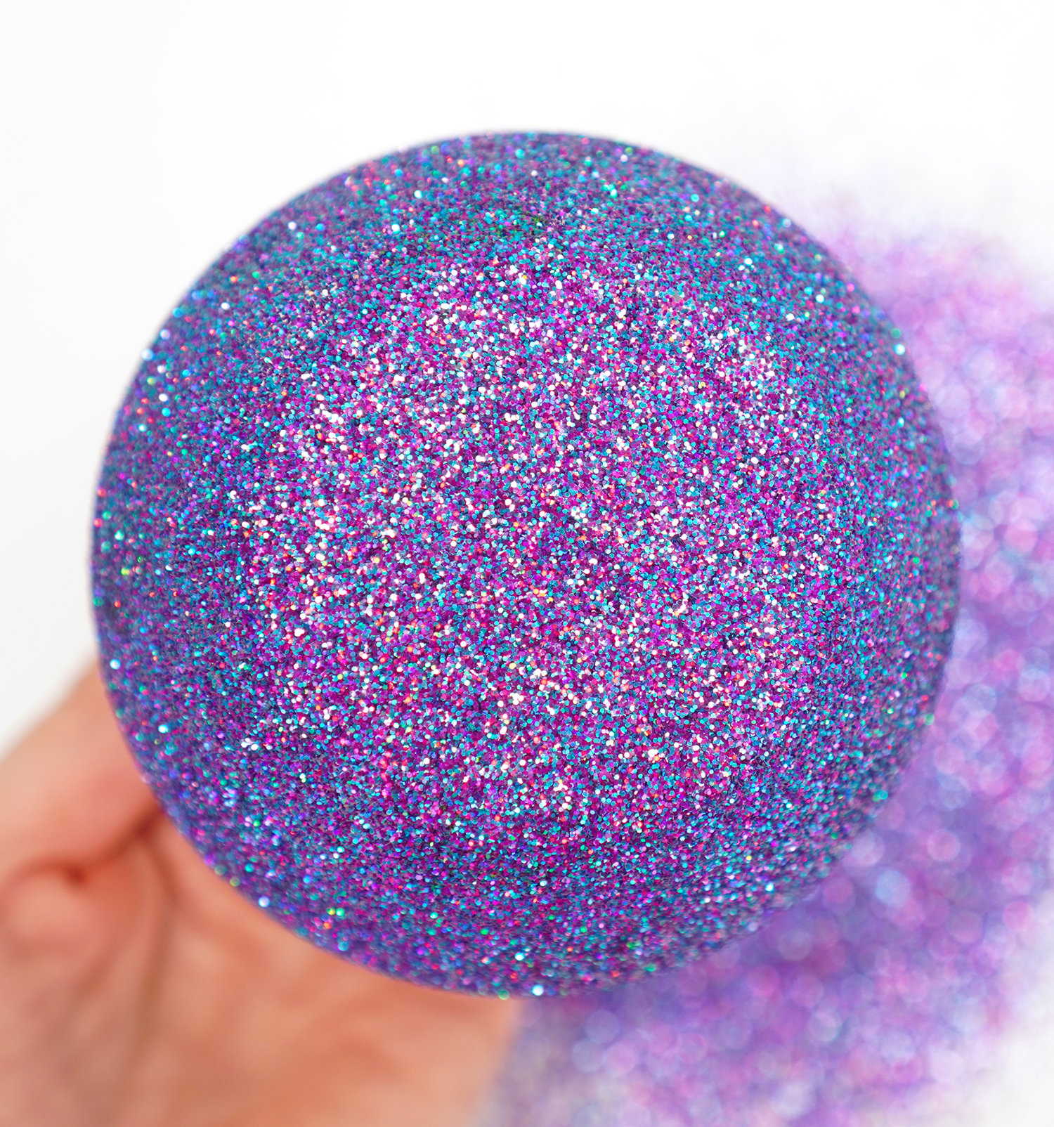 Close up of bottom of wine glass covered in multi-hued purple glitter with shades of fuchsia and turquoise