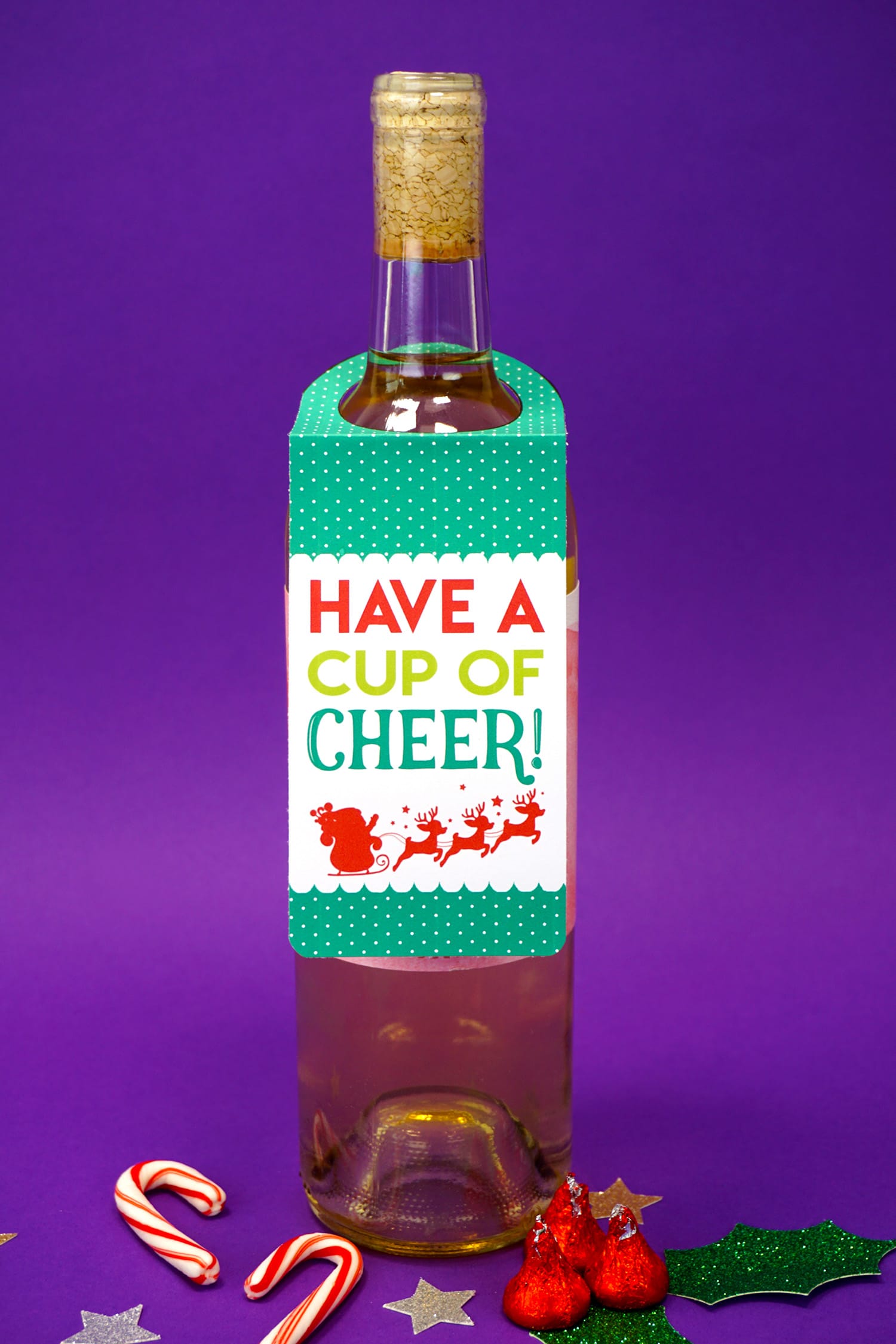 "Have a Cup of Cheer" red, green, and white "Merry Christmas" red, white, and green Christmas wine tag on bottle on purple background with candy canes and stars