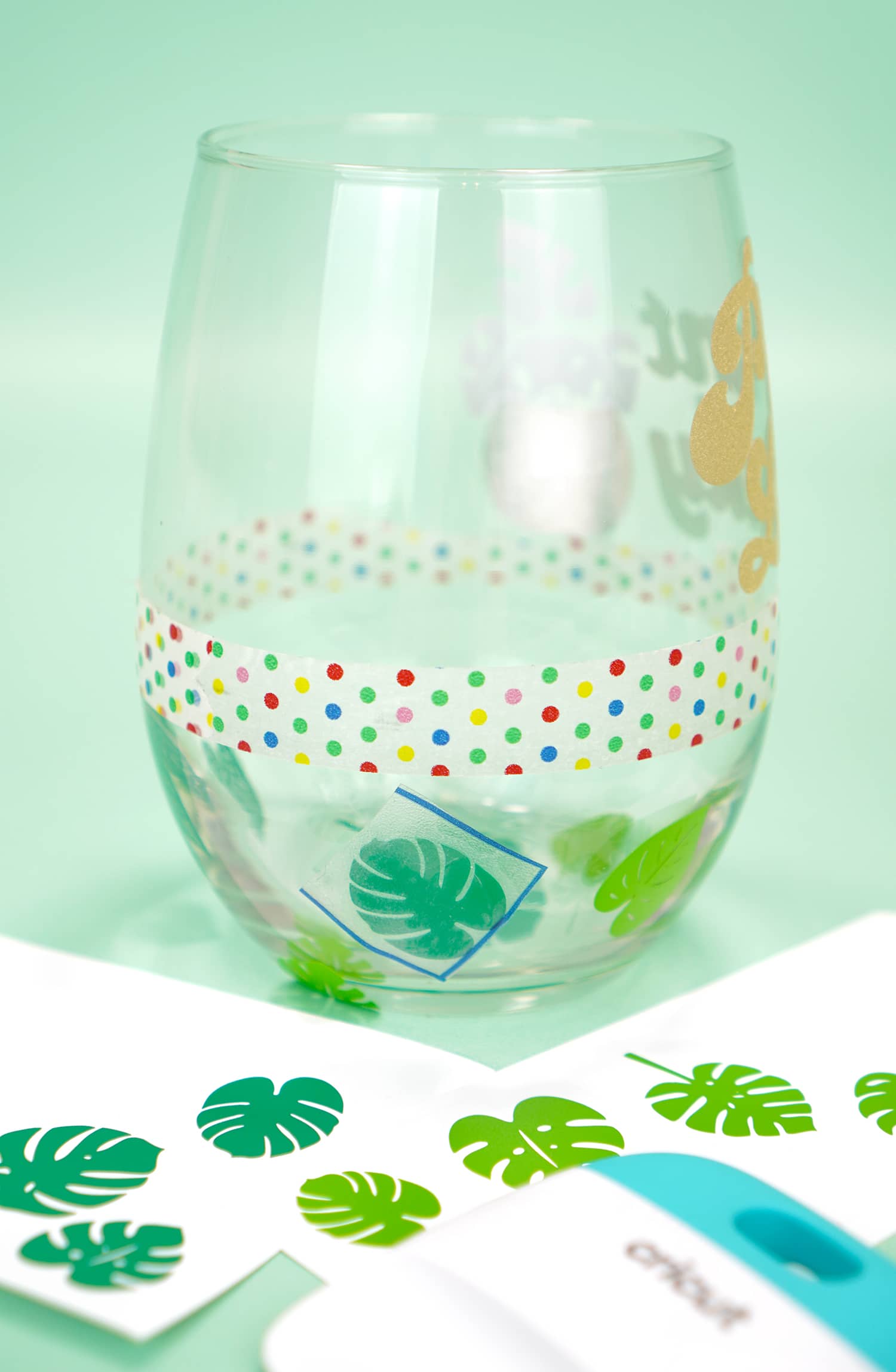 Clear stemless wine glass with band of washi tape and green vinyl leaf decals applied to bottom half of glass