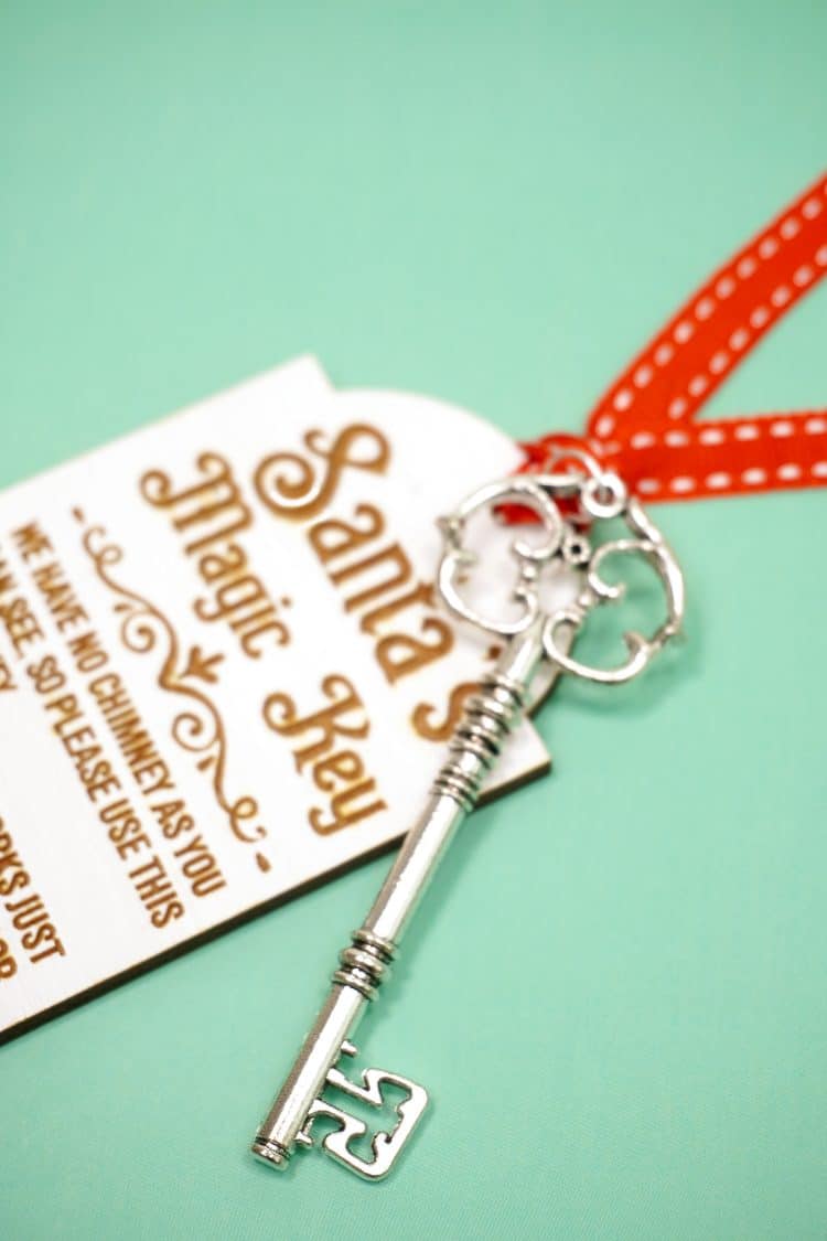 Closeup of silver key attached to a Santa's Magic Key tag with red ribbon on mint green background