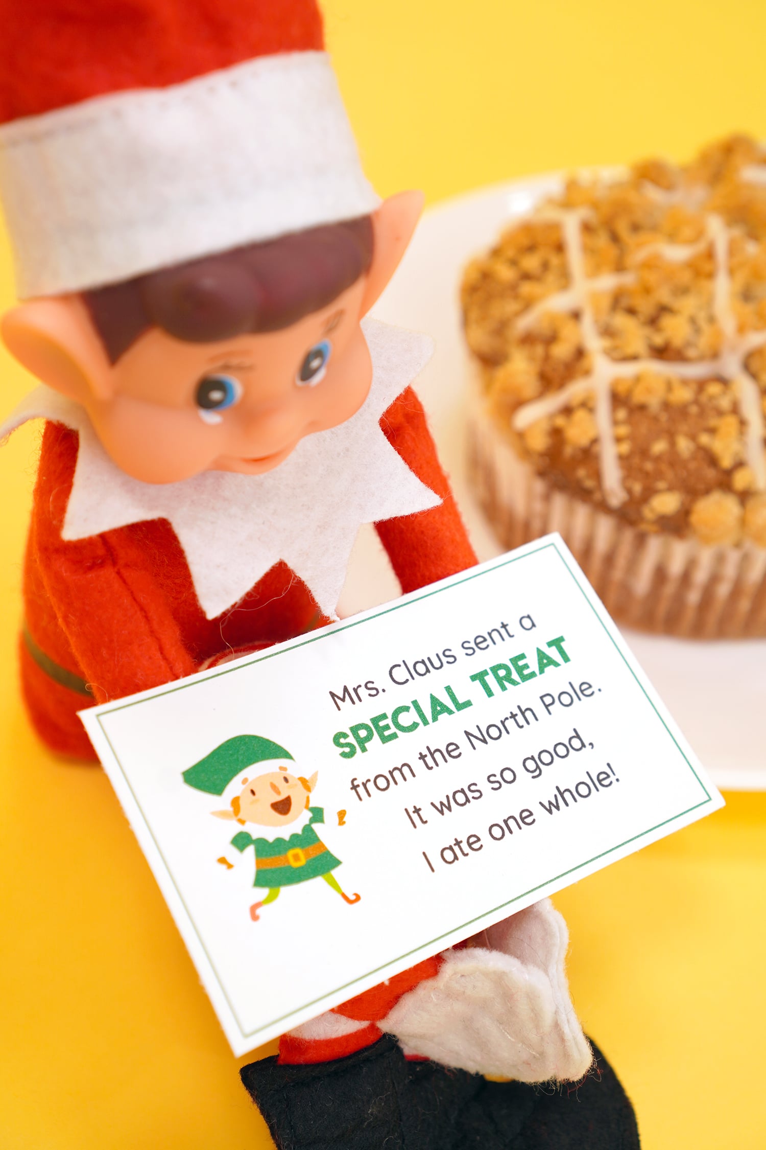Elf on the Shelf doll with printable Elf on the Shelf note card on yellow background with bakery treats in the far background