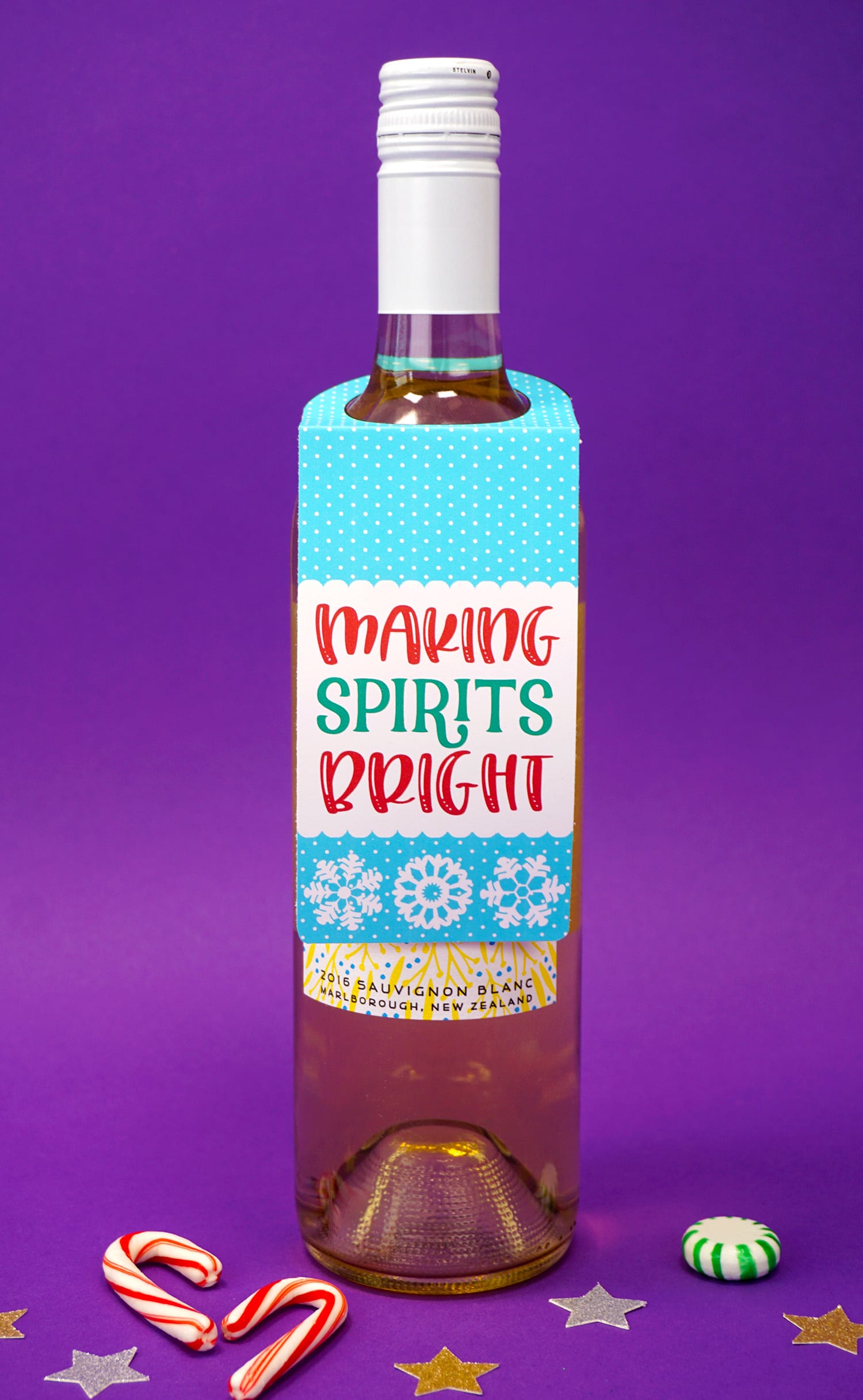 "Making Spirits Bright" Christmas wine tag on bottle on purple background with candy canes and stars