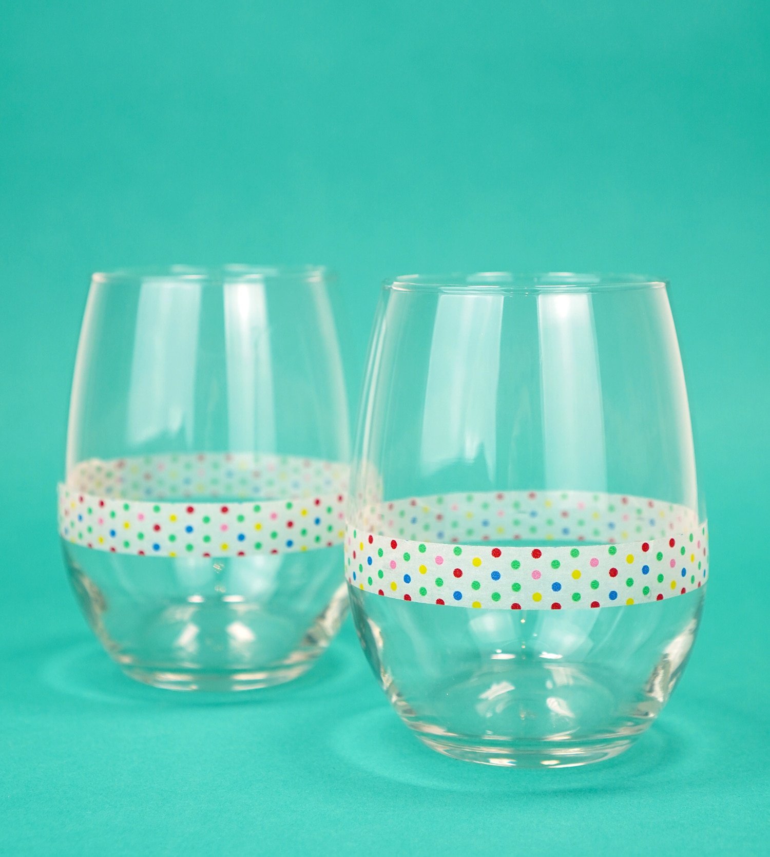 Two stemless wine glasses on teal background with a band of polka dot washi tape around each glass