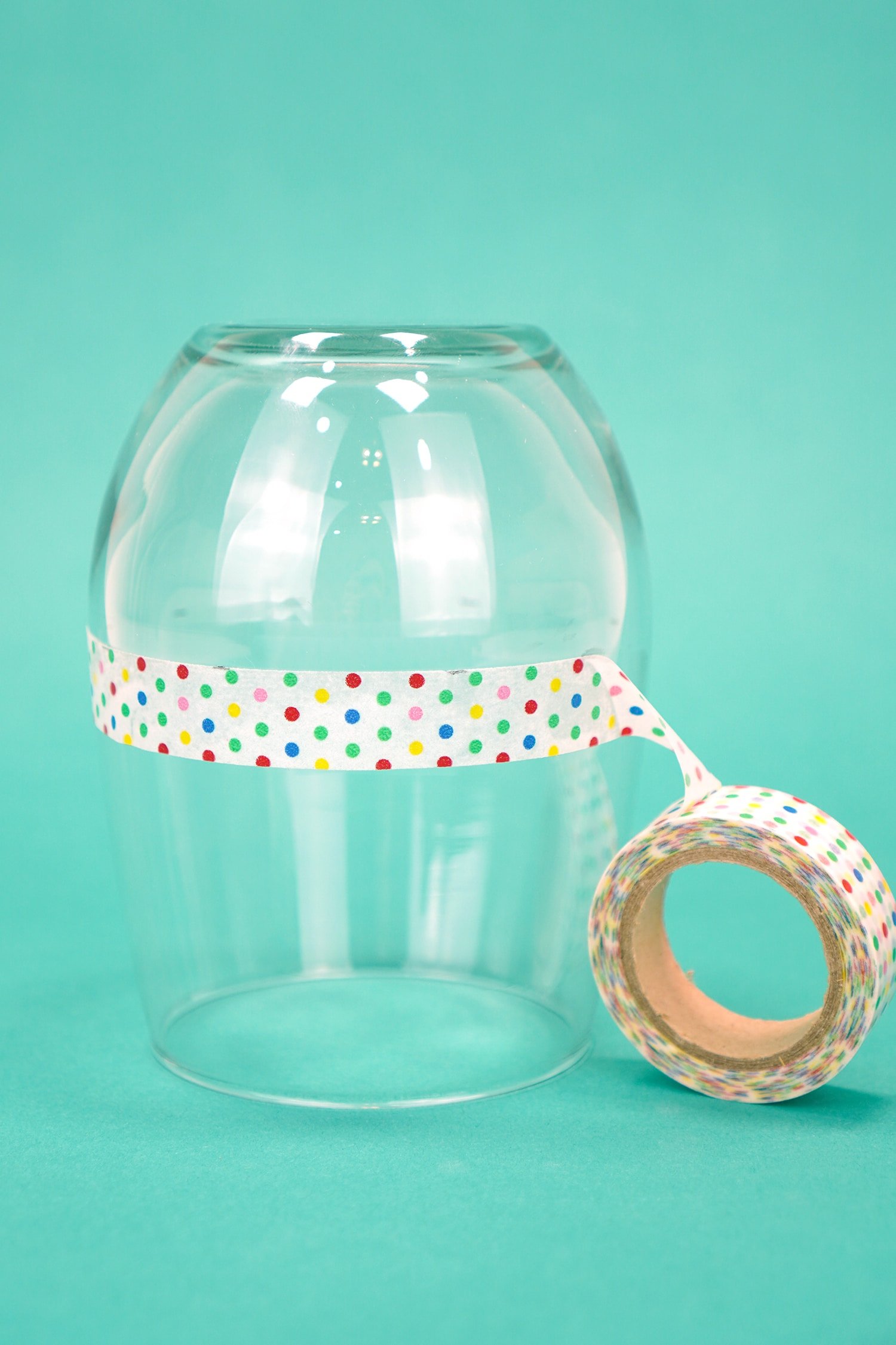 Upside down stemless wine glass on teal background with a ring of polka dot washi tape around glass