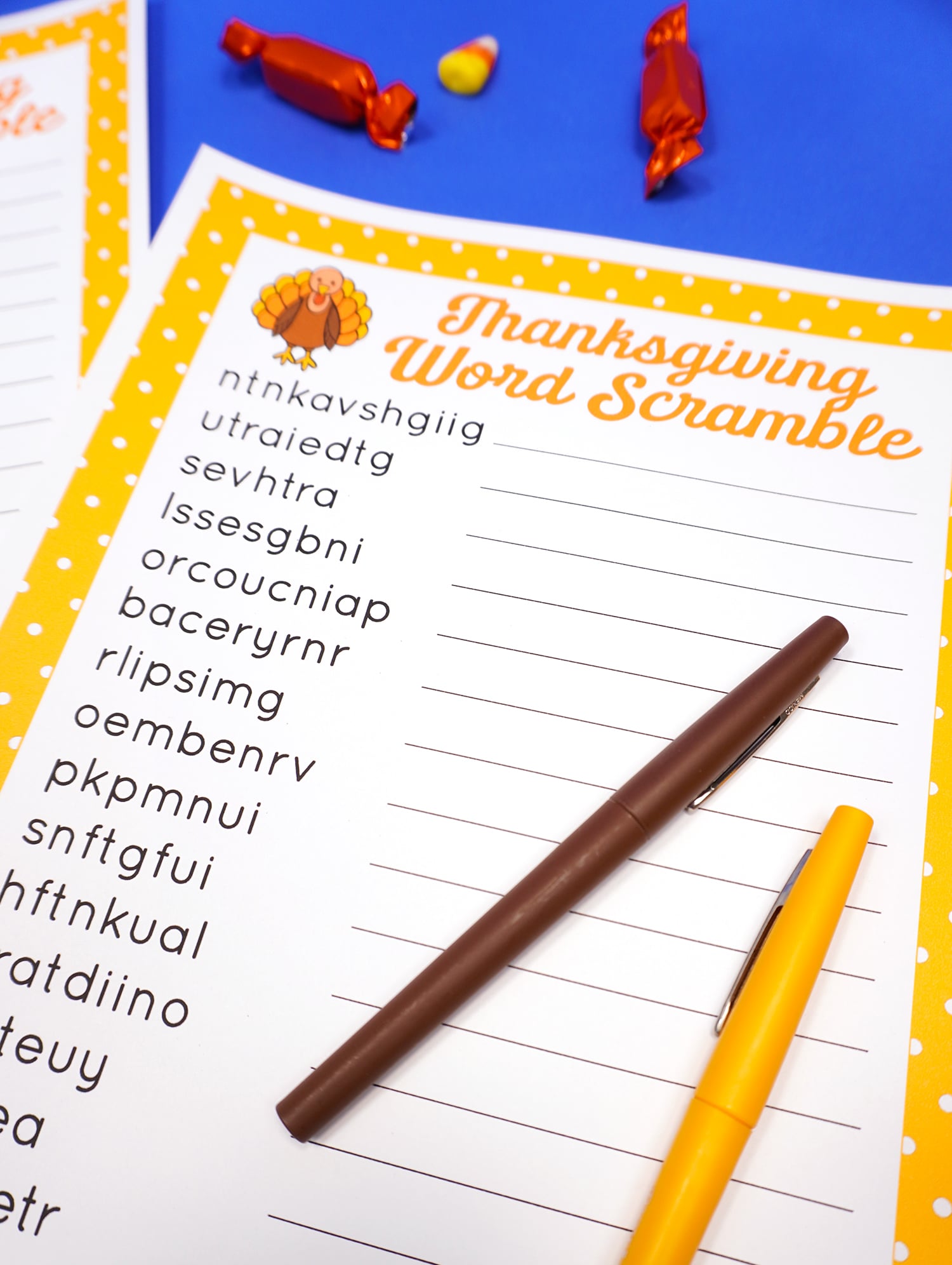 Close up of printable Thanksgiving Word Scramble on a blue background surrounded by candy and a yellow and brown pen. 