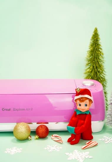 Vintage Elf in front of pink Cricut Explore Air machine on mint background with ornaments and bottle brush trees