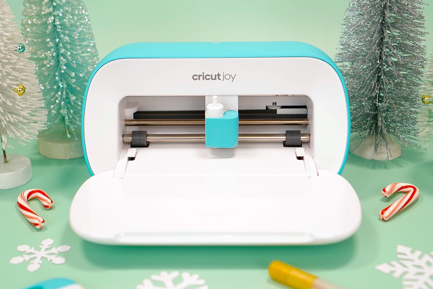 Cricut Joy machine with bottle brush trees, paper snowflakes, and candy canes on mint green background