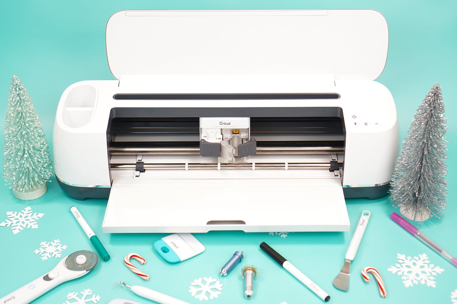 Cricut Maker machine on aqua background surrounded by scattered Cricut tools and mini candy canes