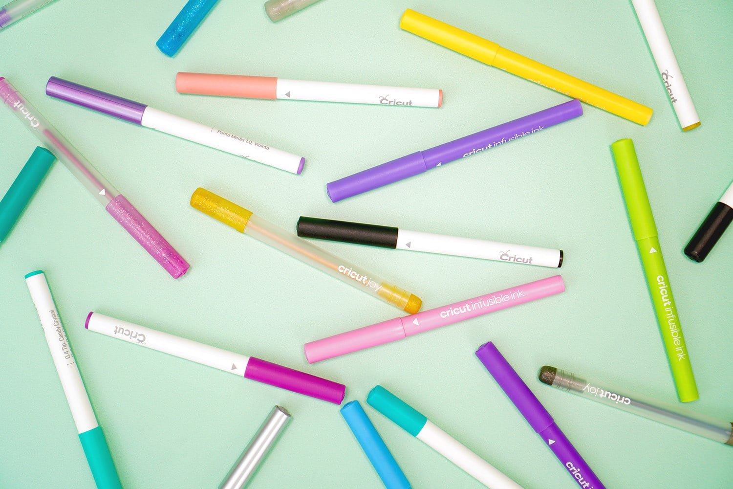 Various Cricut pens and markers scattered on a mint green background