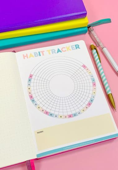 Printable Circle Habit Tracker in bullet journal on pink background with colorful pencils and stack of journals