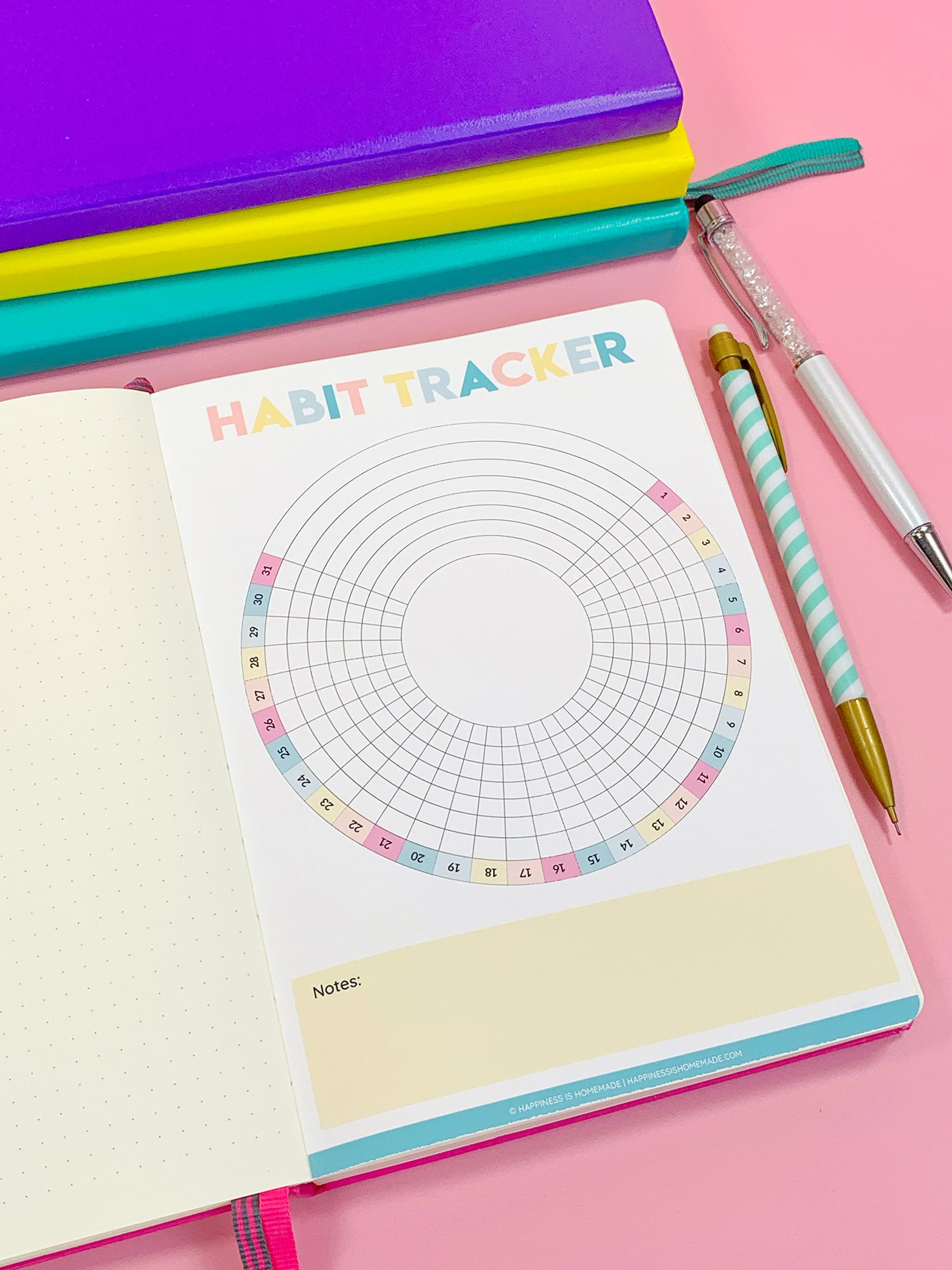 Printable Circle Habit Tracker in bullet journal on pink background with colorful pencils and stack of journals