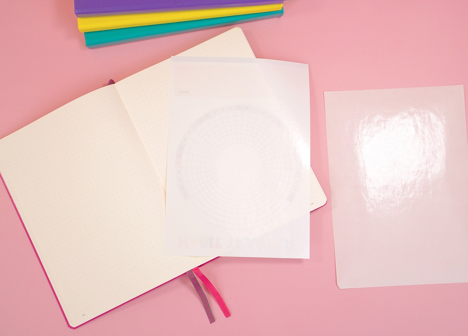 Open bullet journal on pink background with peeled sheet of sticker paper on top