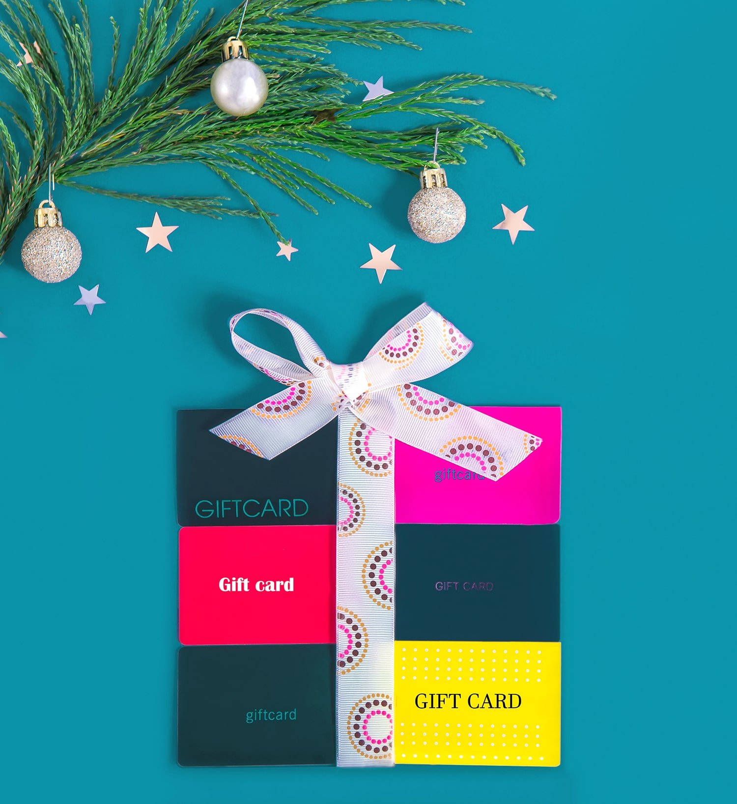 Flat lay gift box shape made of shop gift cards and tied with a ribbon on a blue background with Christmas tree branch