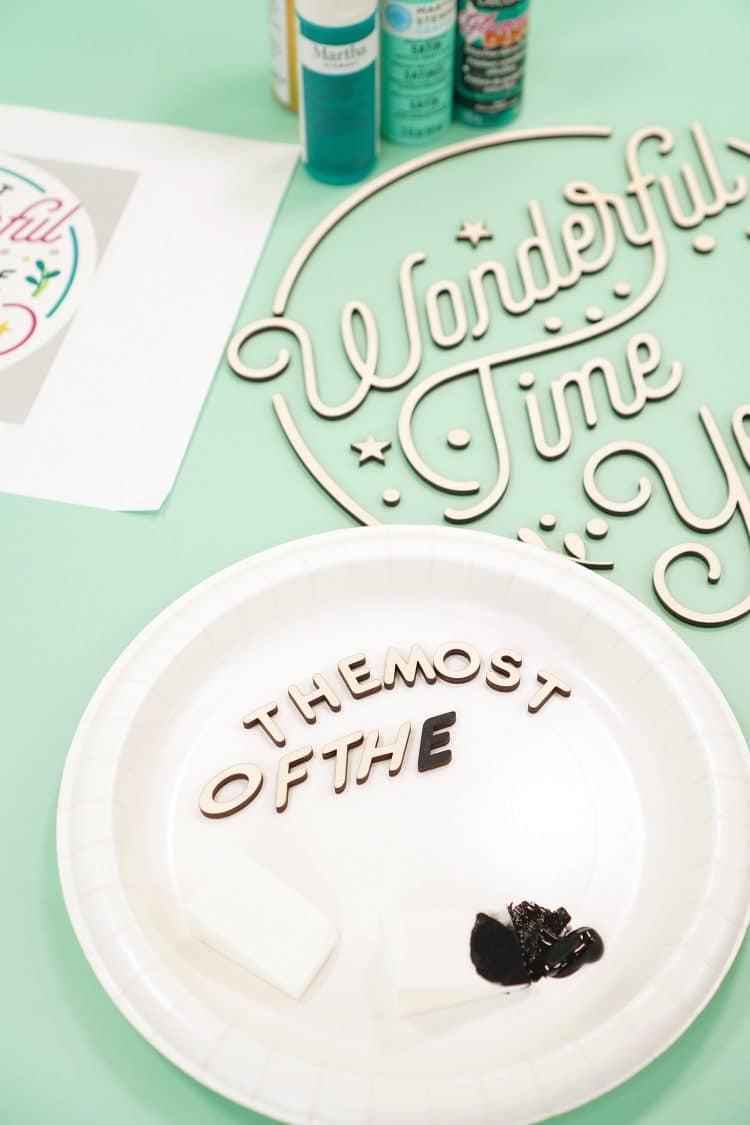 White paper plate with black paint and cosmetic sponges with Glowforge laser cut wood pieces and bottles of paint in background