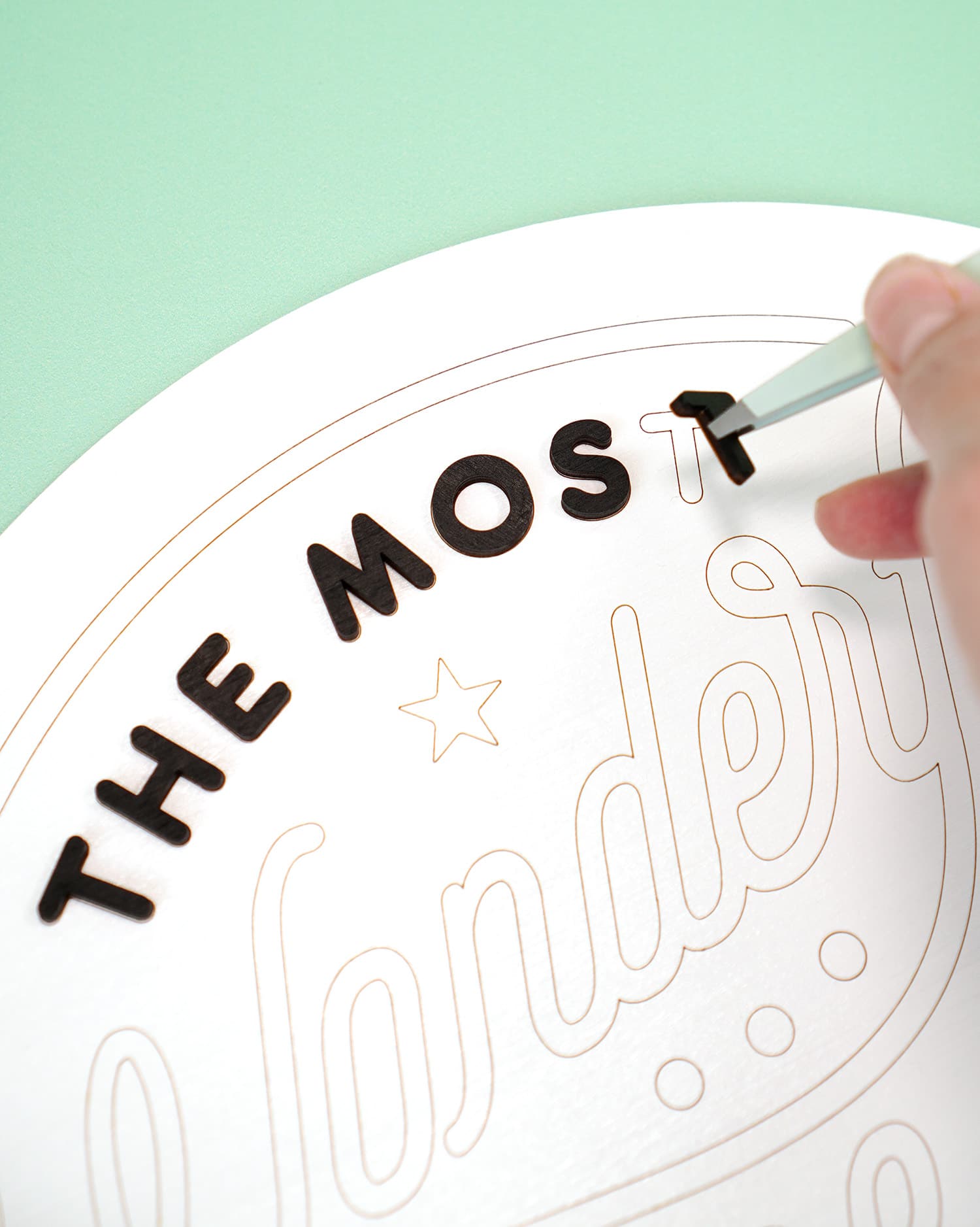 Close up of laser cut wood sign pieces being placed on sign with tweezers