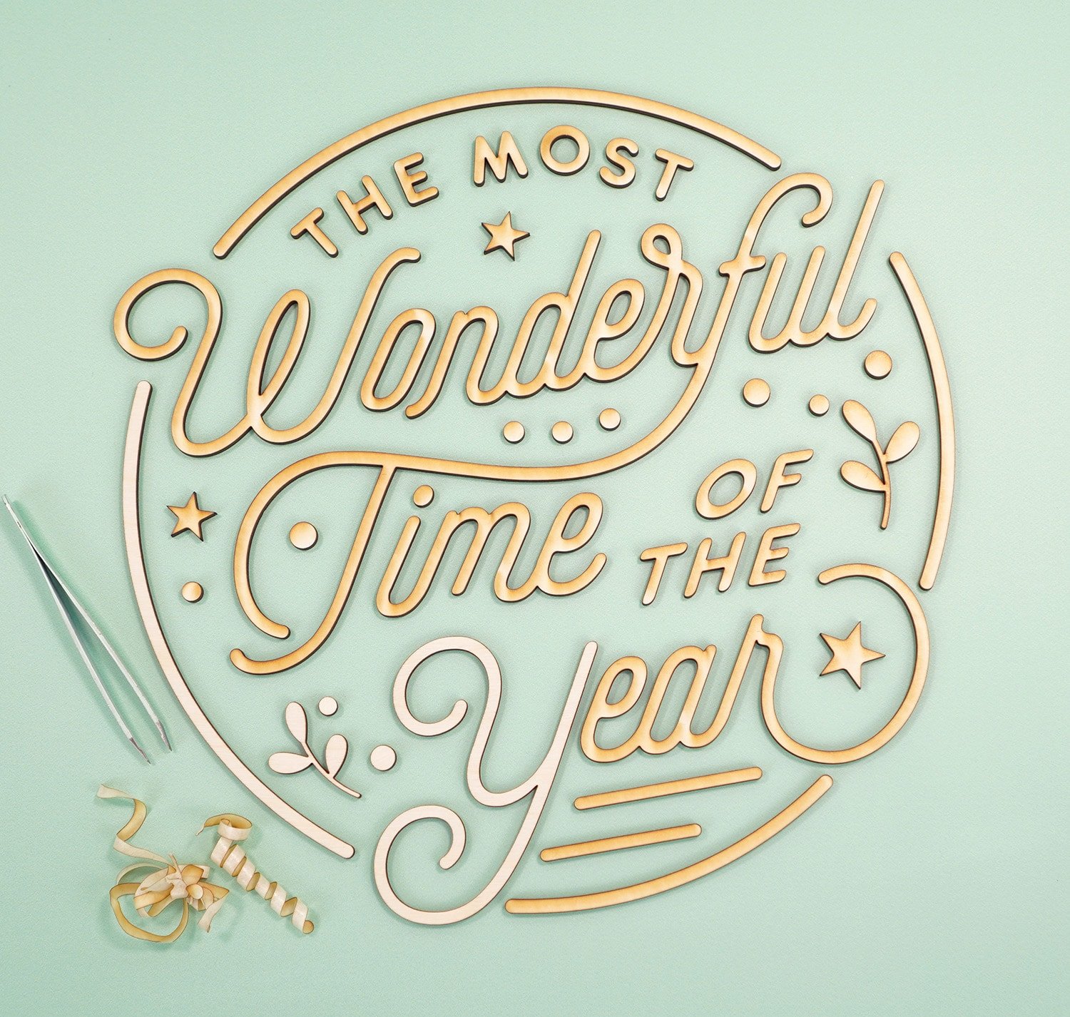 "The Most Wonderful Time of the Year' Laser Cut Wood Sign pieces with tweezers and pile of peeled off masking tape on mint green background