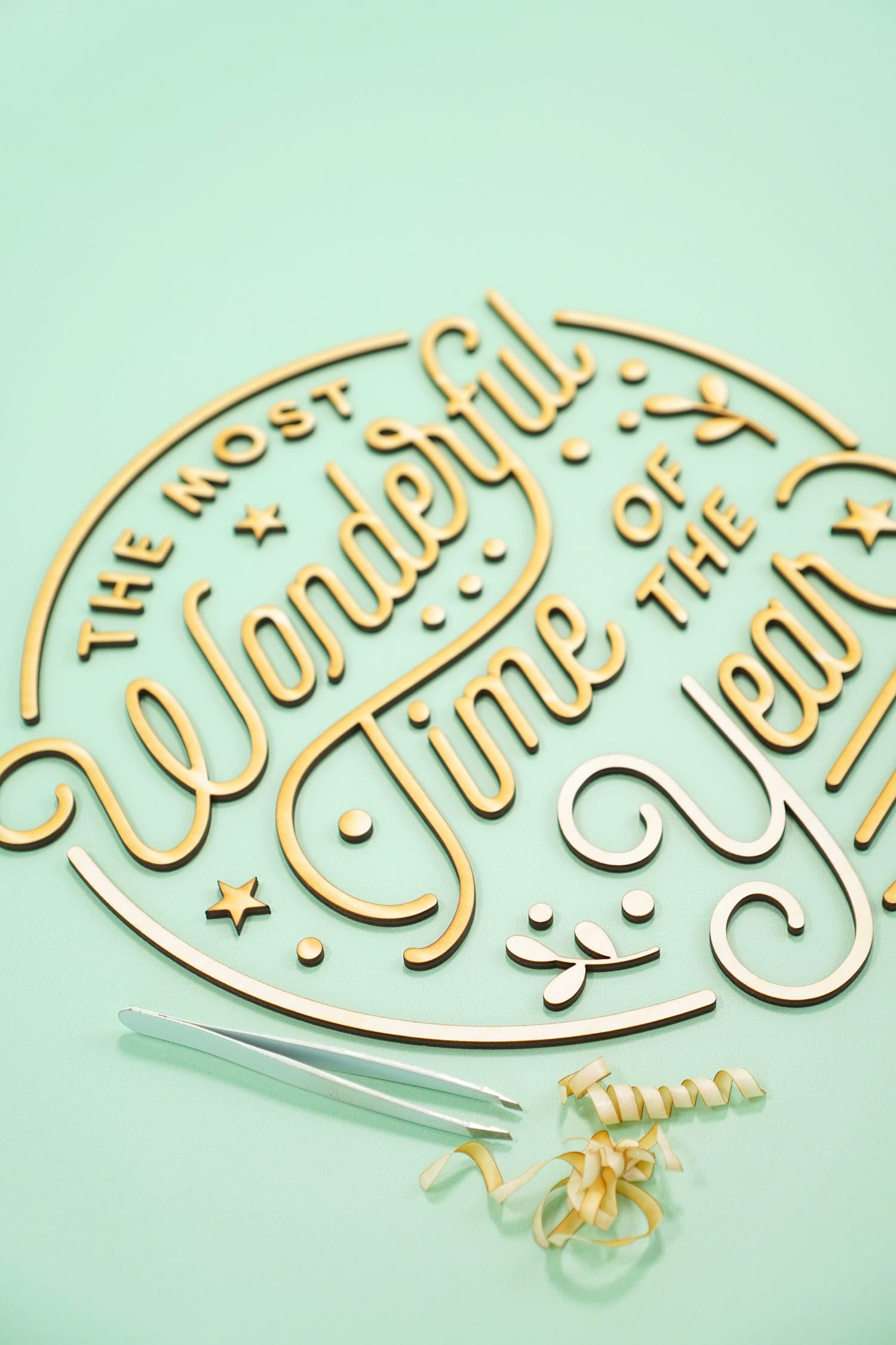 "The Most Wonderful Time of the Year' Laser Cut Wood Sign pieces with tweezers and pile of unmasked masking paper tape on mint green background