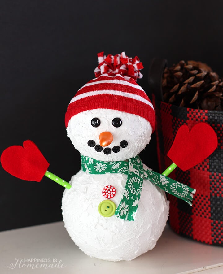 snowman holiday decoration sitting in front of festive bucket of pine cones