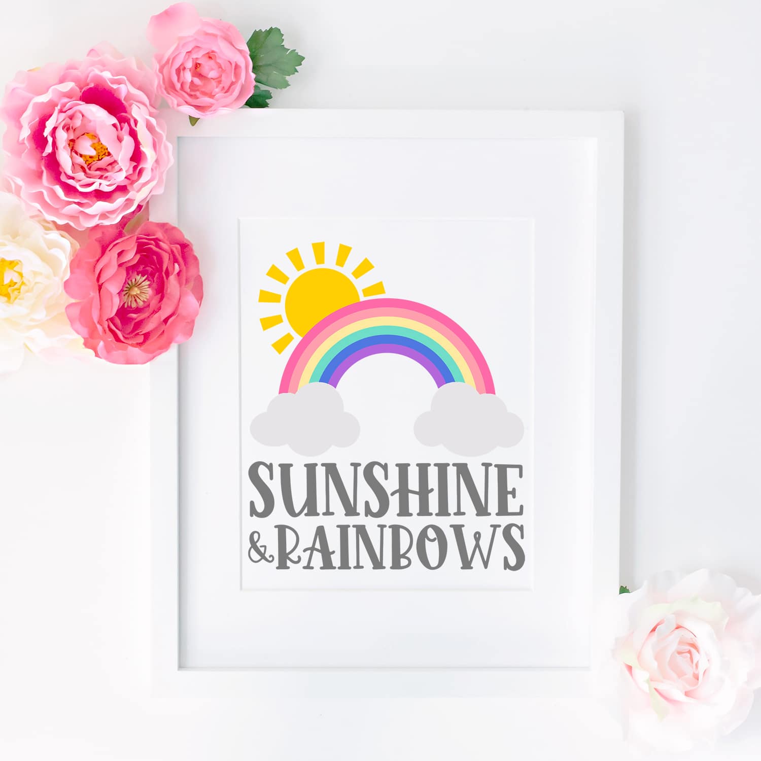 "Sunshine and Rainbows" artwork in a white frame surrounded by pink and yellow flowers
