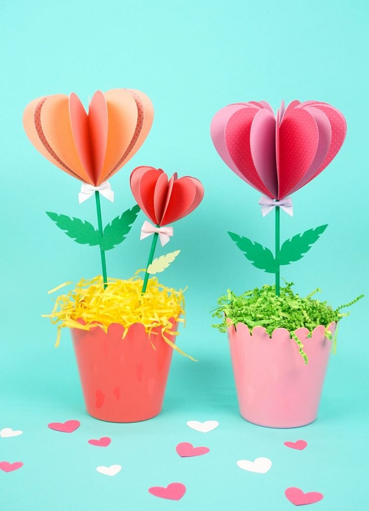 Three pink paper flowers in two pots on turquoise background