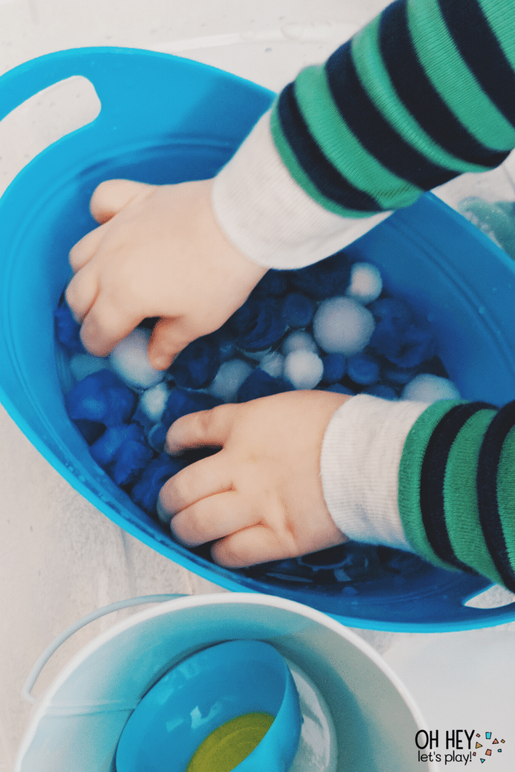 child soaking pom poms in sensory bin