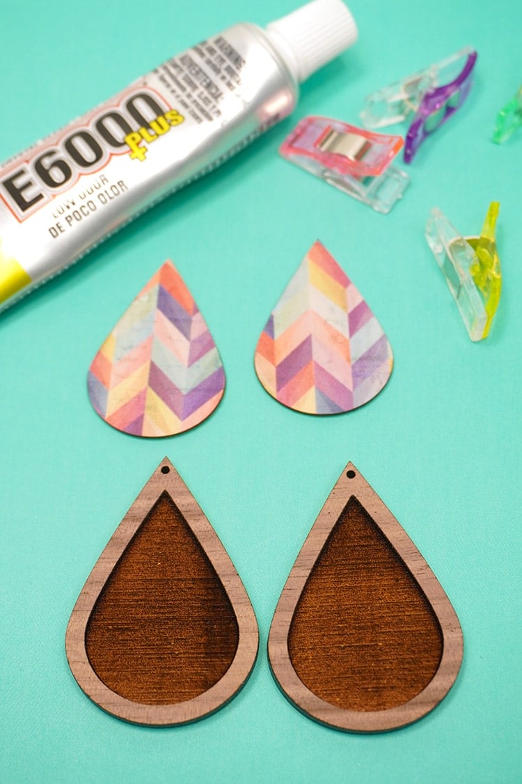 Wood teardrop earrings with cork teardrop inlay pieces, glue, and clamps on teal background