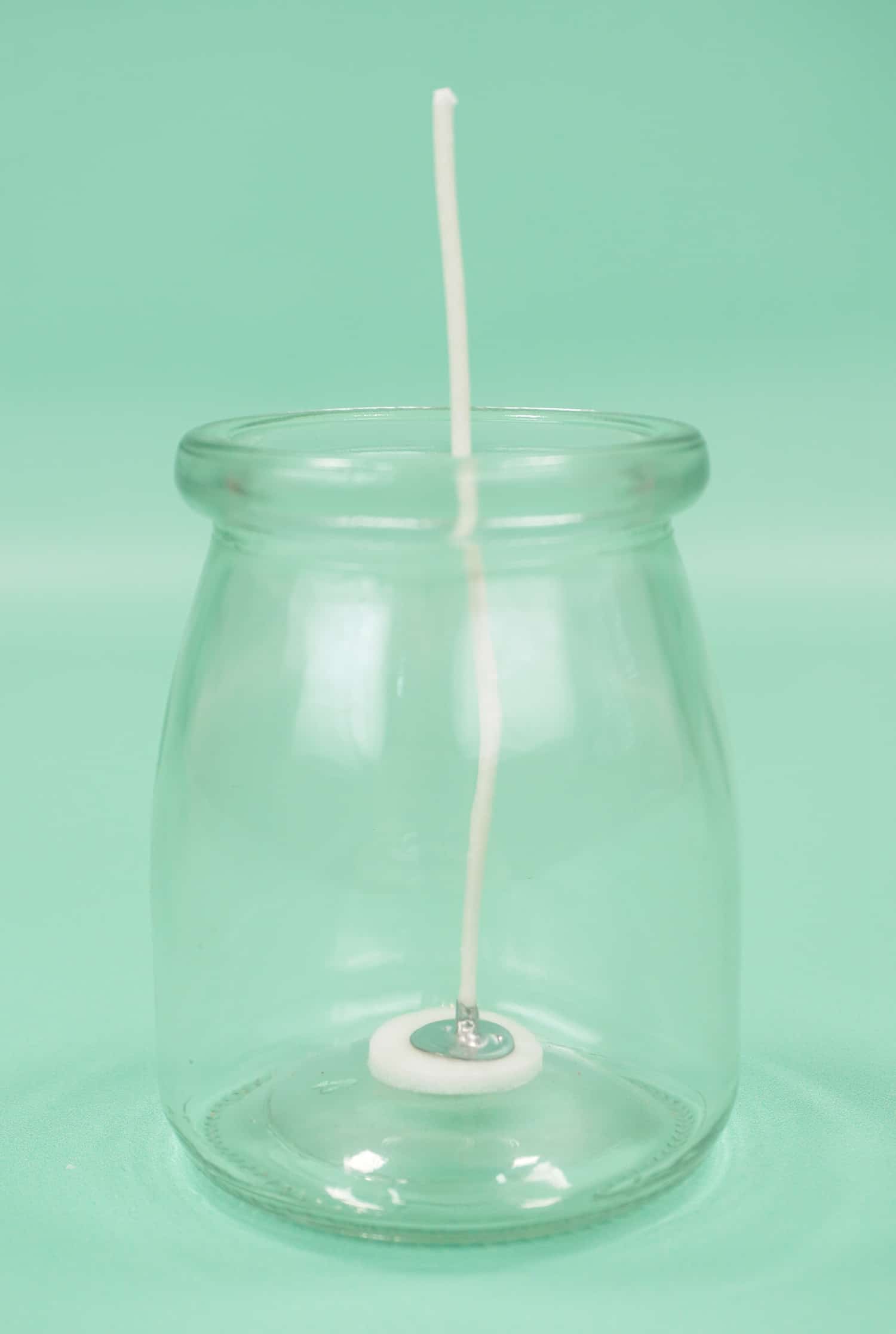 Empty glass jar with candle wick on mint green background
