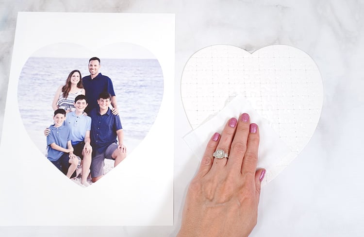 Hand with cloth cleaning off heart shaped puzzle blank on marble background