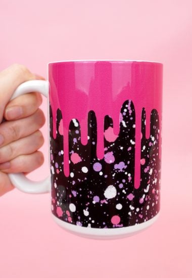 Hand holding pink and black "drippy" mug on a pink background