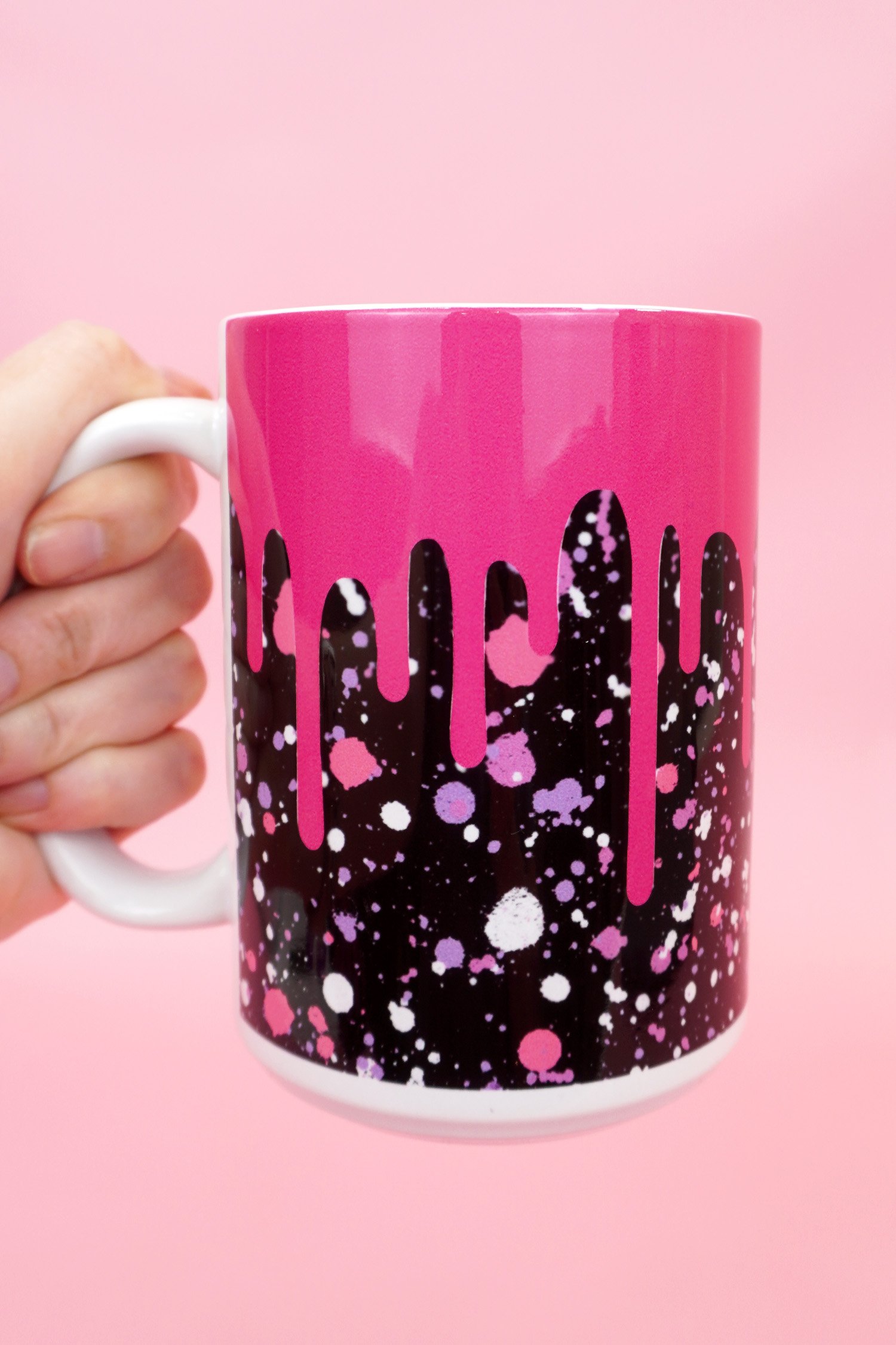 Hand holding pink and black "drippy" mug on a pink background