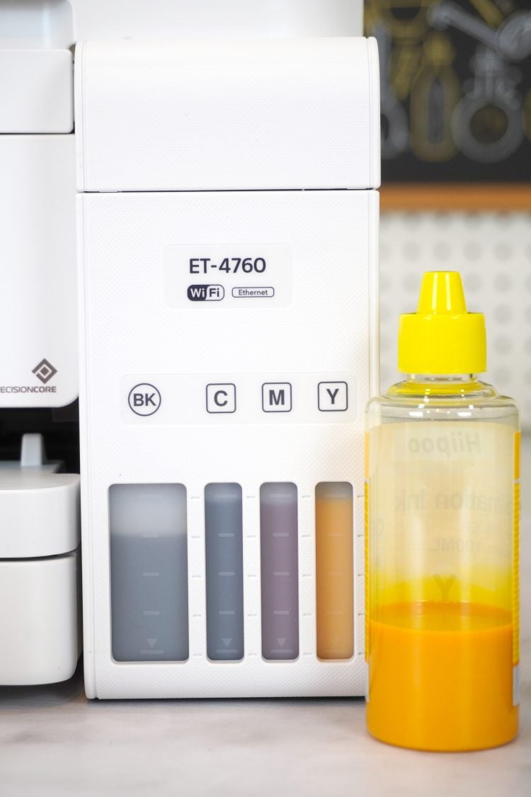 partially empty bottle of yellow sublimation ink in front of full Epson EcoTank ink tanks