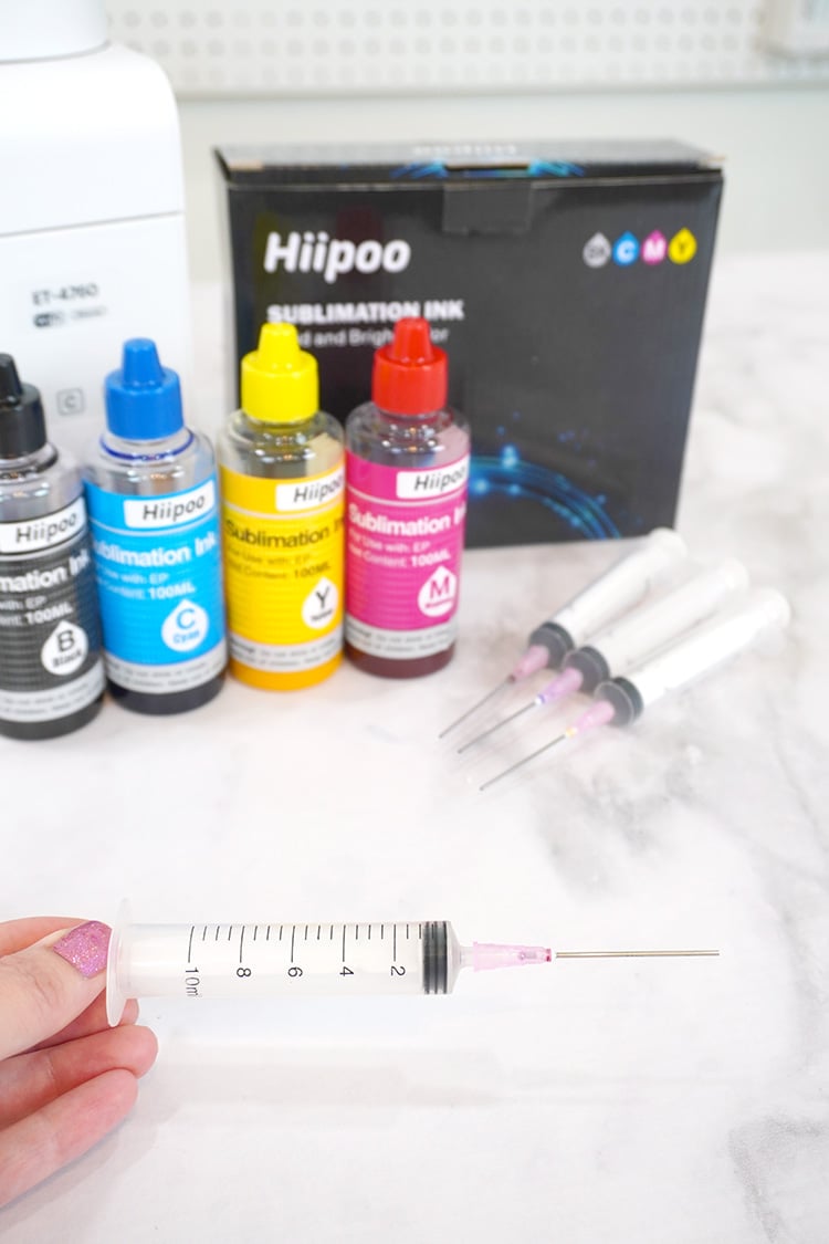 Close up of plastic syringe with blunt needle tip and bottles of sublimation ink in background