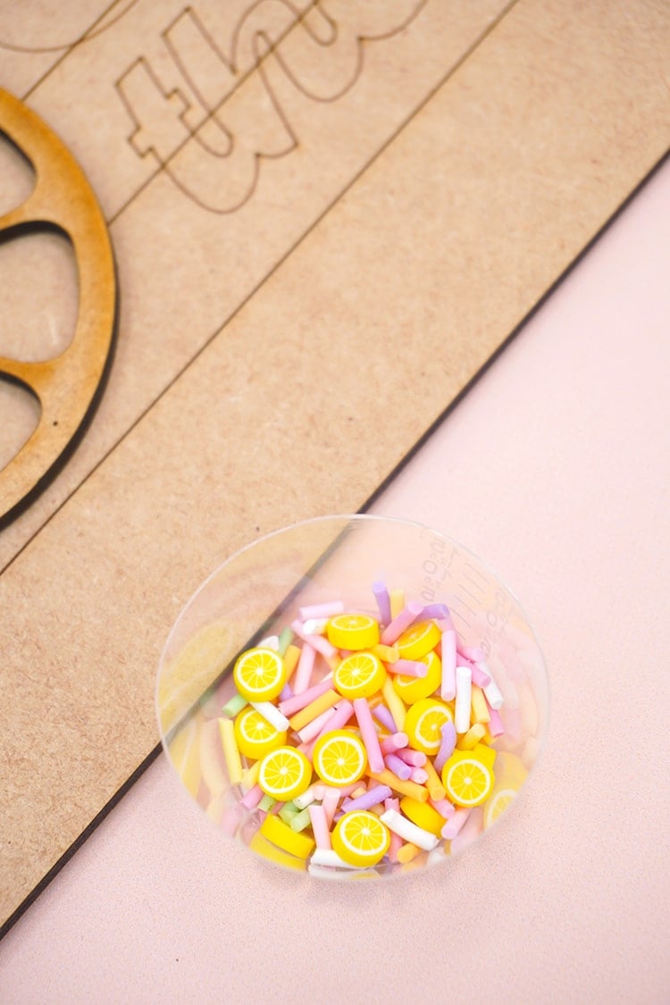 Small clear cup of polymer clay lemon slices and sprinkles on peach background