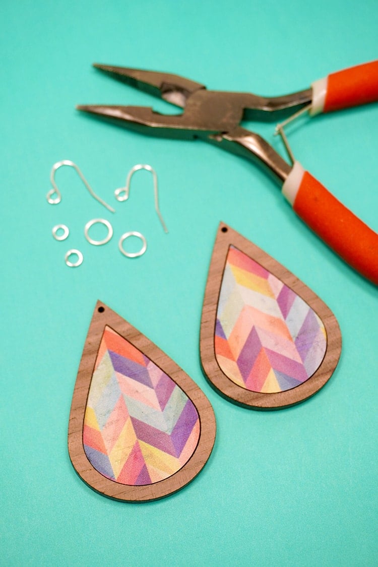 Two cork and wood teardrops on a teal background with silver jewelry hardware and pliers