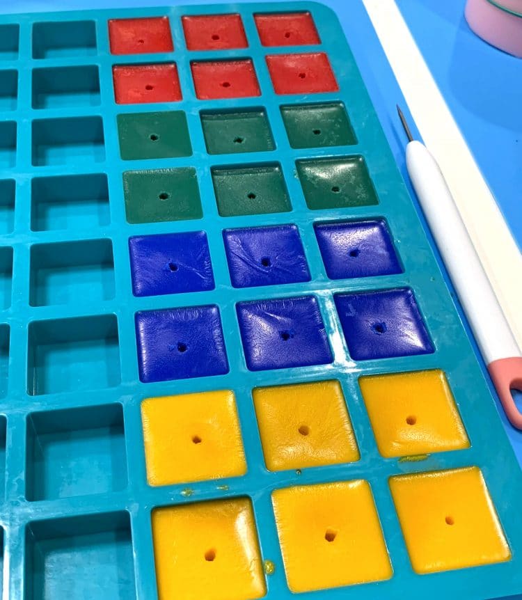 Red, green, blue, and yellow wax cubes with small center holes in silicone mold