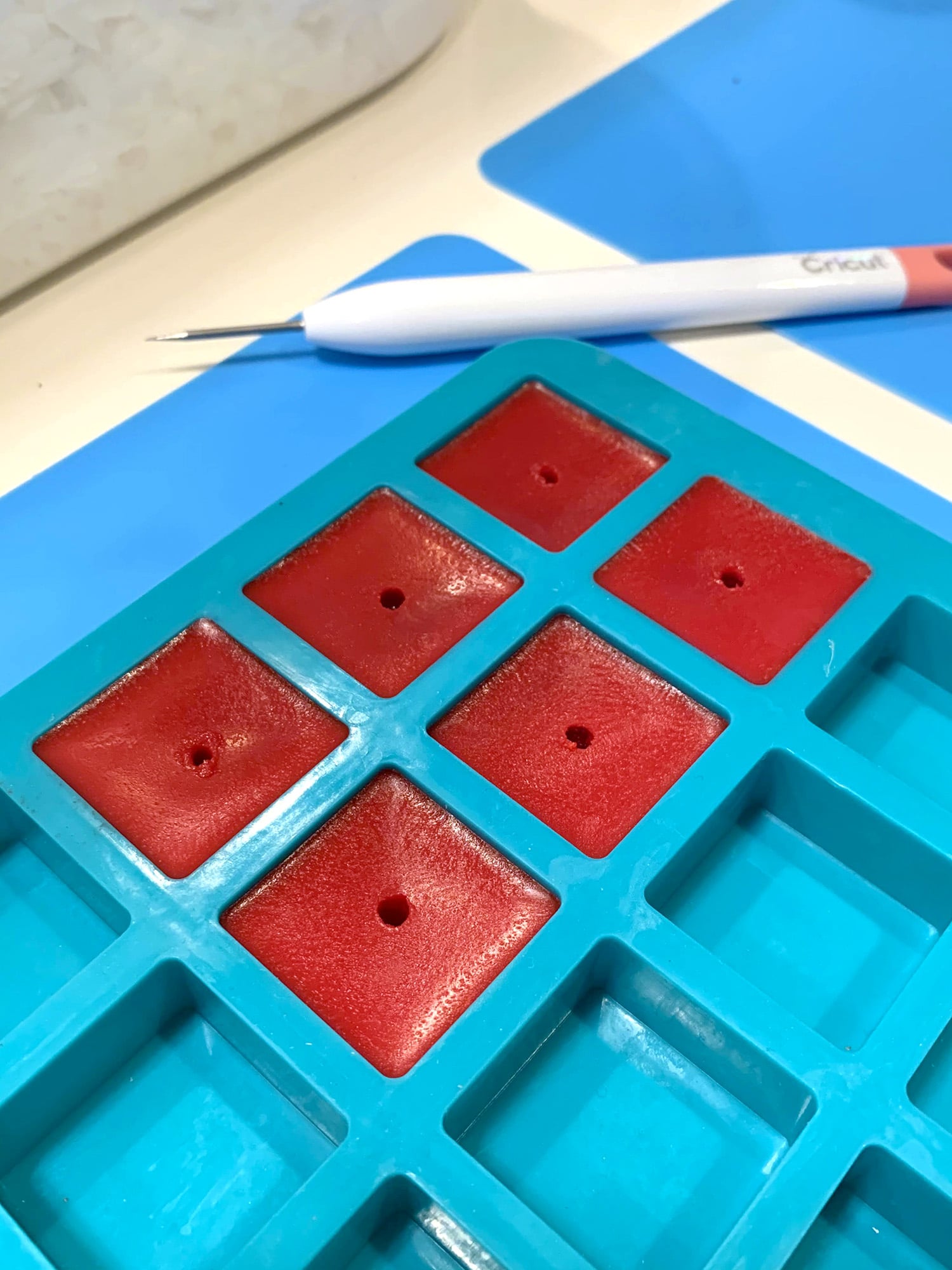 Red wax cubes with small center holes in silicone tray with awl tool in background