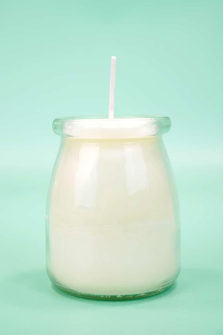 White candle in glass jar on mint green background