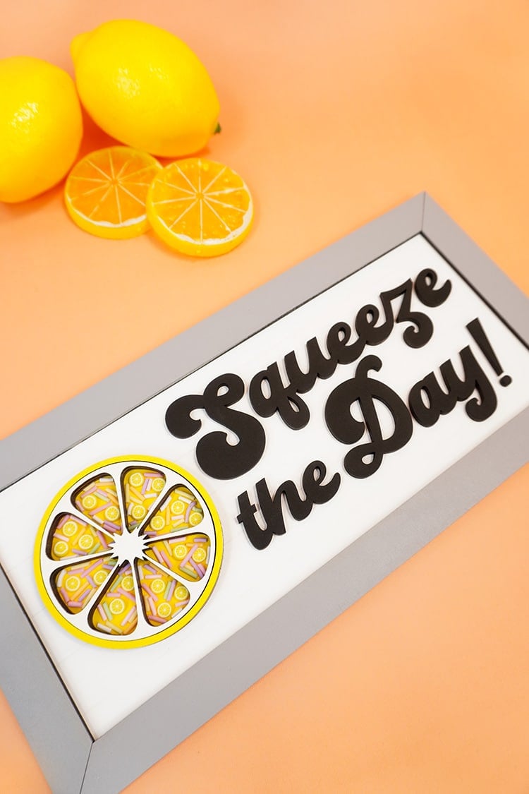 Squeeze the Day sign on an orange background with lemons