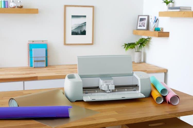 Cricut Explore 3 on wood work table surrounded by assorted rolls of vinyl materials