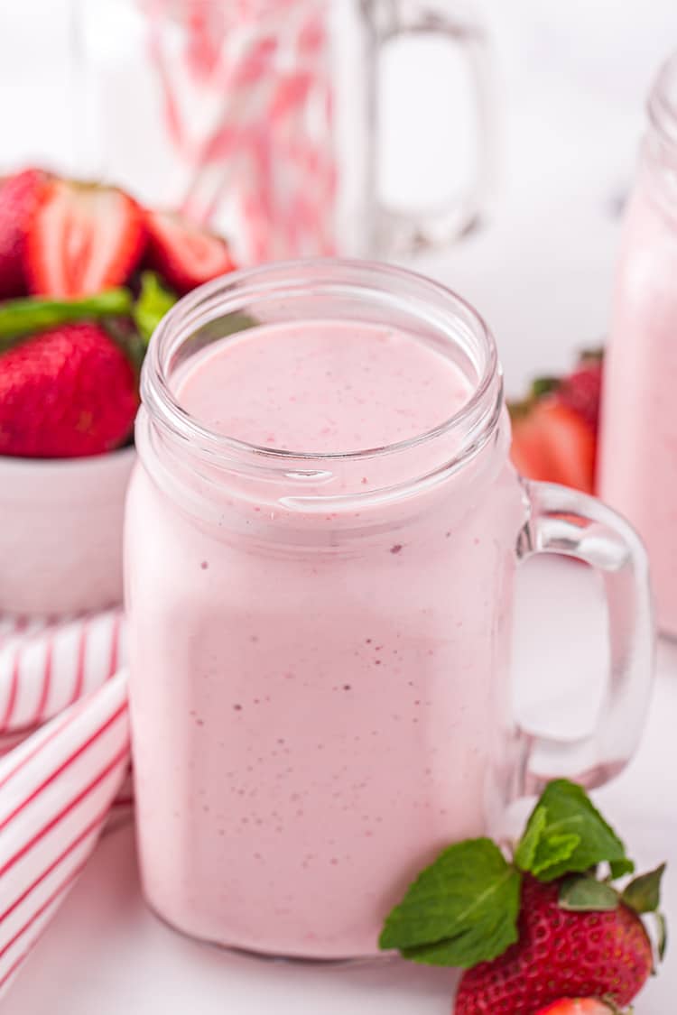 Freshly poured pink strawberry milkshake in glass mason jar mug
