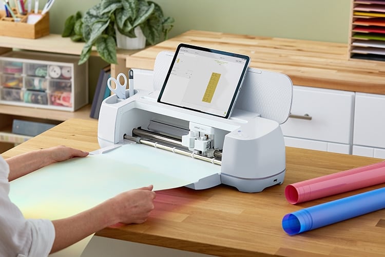 tablet on top of cricut machine with hand pulling material from machine