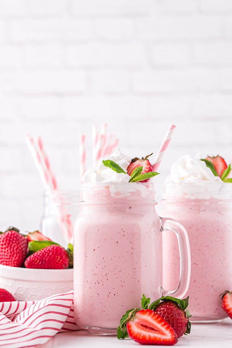 Yummy strawberry milkshakesin glass mugs with whipped cream and strawberry garnish and pink striped straws