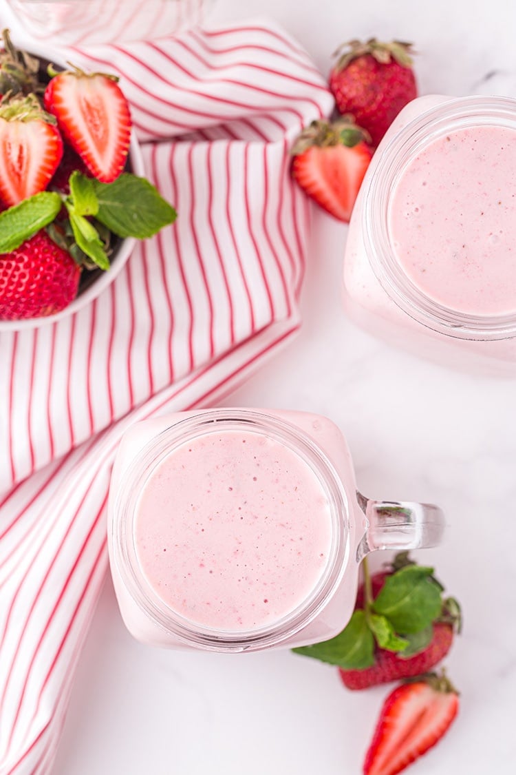 Overhead view of two strawberry milkshakes in glass mugs