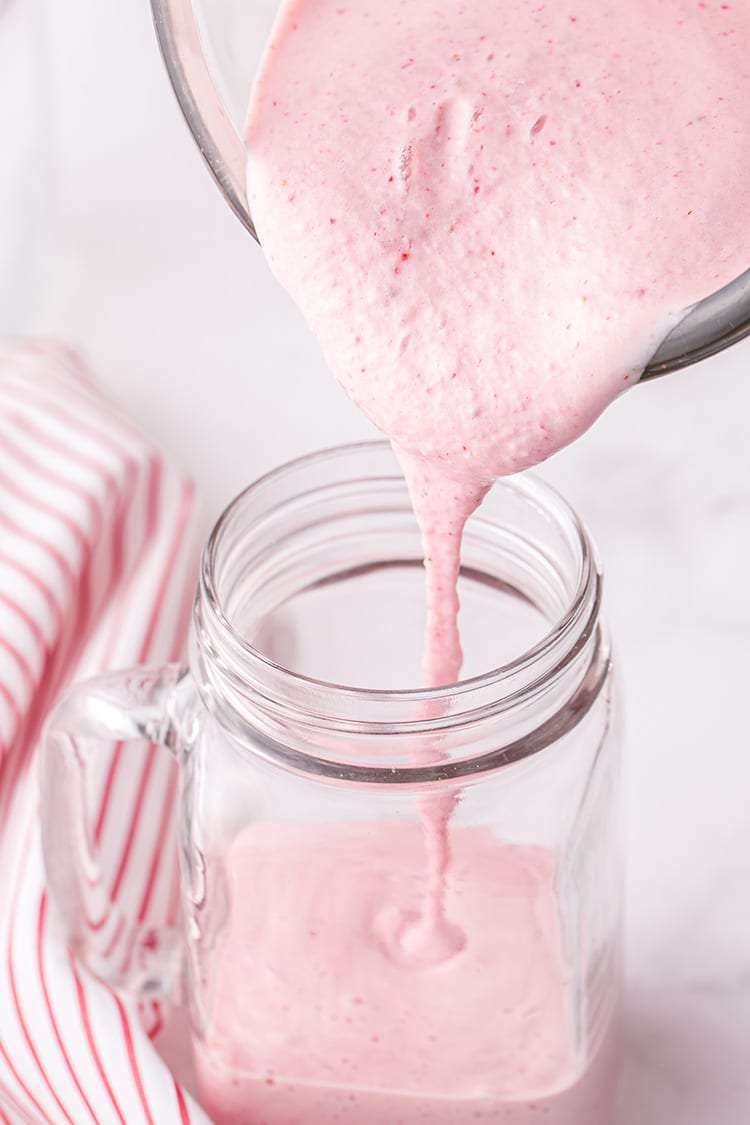 Pouring a Strawberry Milkshake from a glass blender into a glass mason jar mug