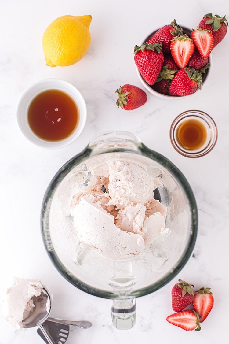 Strawberry ice cream in blender surrounded by other strawberry milkshake ingredients