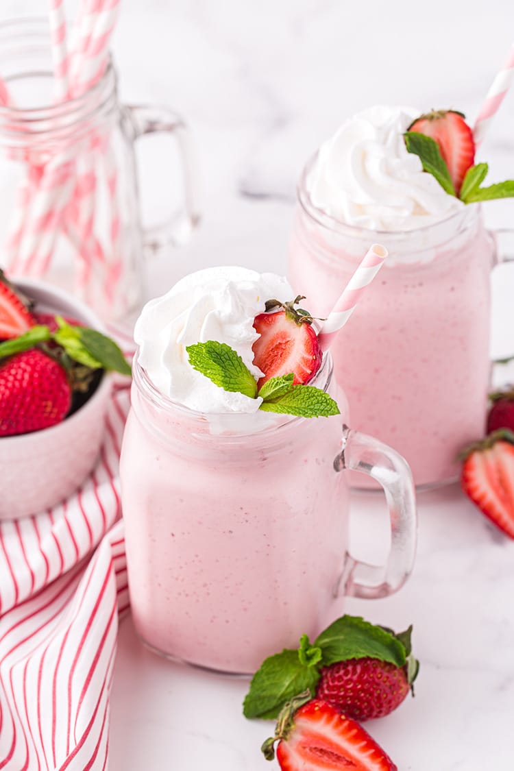 Glass mug filled with pink strawberry milkshake with whipped cream and strawberry garnish