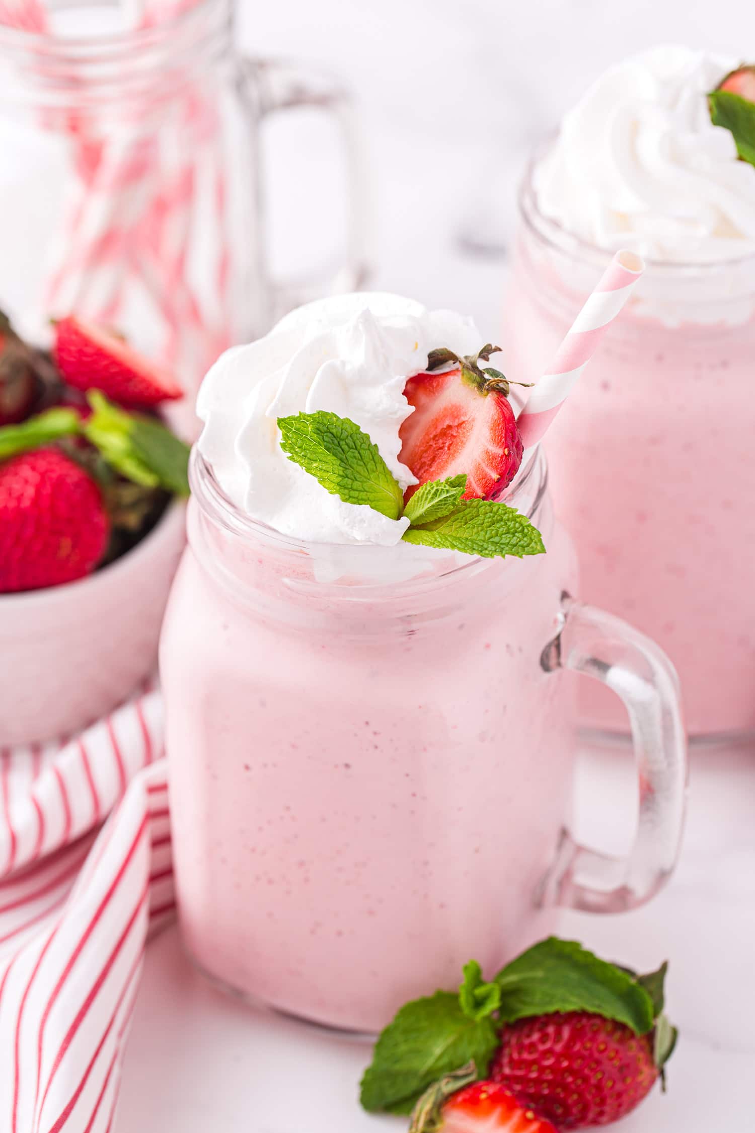 Strawberry milkshake in glass mug with whipped cream, strawberry, and mint leaf garnish