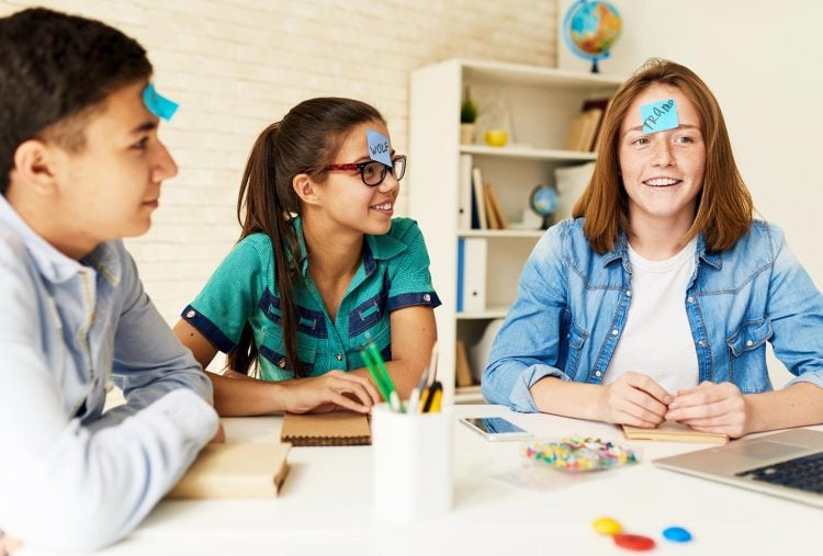 3 teenage kids with blue sticky notes on their forehead playing a game
