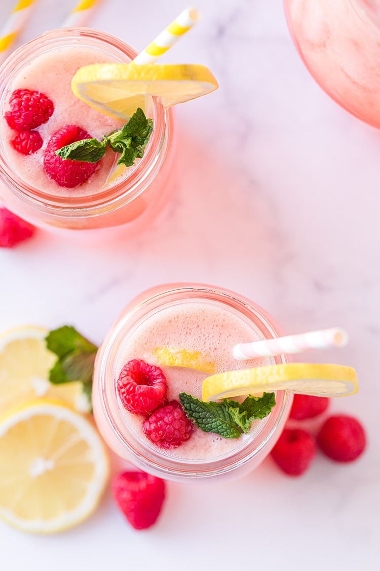 Overhead view of fresh raspberry, lemon, and mint sprig garnish in a glass of homemade raspberry lemonade