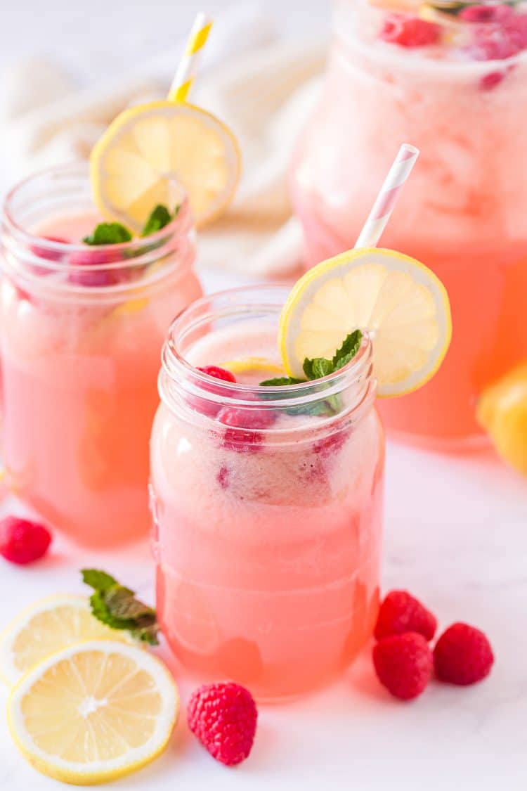Two mason jar glasses of homemade raspberry lemonade with lemon wheels, mint sprigs, and fresh raspberries
